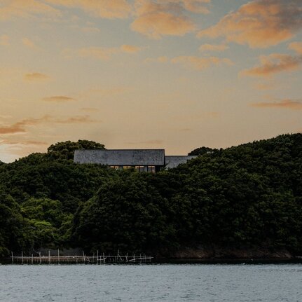 Amanemu resort perched on forested hillside at sunset overlooking calm waters, Japan.