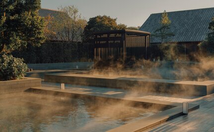 安缦伊沐度假村的温泉池，晨雾升腾，传统建筑在背景中。