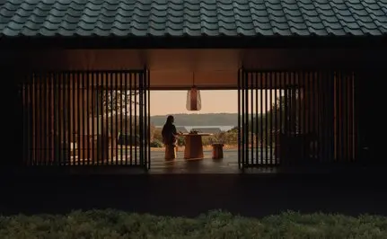 Amanemu resort's welcome pavilion with wooden sliding doors opening to an illuminated interior courtyard at dusk, Japan.
