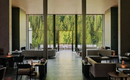 Bright dining room at Aman Rosa Alpina with floor-to-ceiling windows overlooking alpine greenery, black dining tables, and minimal décor.