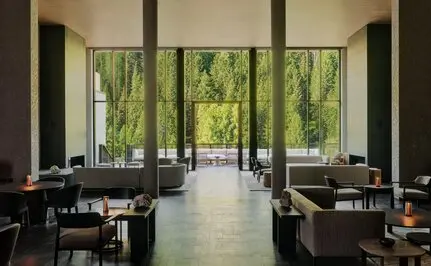 Dining venue at Aman Rosa Alpina resort with floor-to-ceiling windows framing Alpine views, dark dining tables, and natural light.