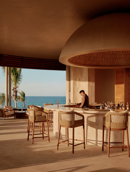 Amanvari's lounge bar with curved wooden architecture, comfortable seating, and expansive views over the Mexican landscape at sunset.