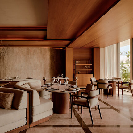 Amanvari principal bedroom with wooden beams, stone accent wall, and adjoining sitting area with views.