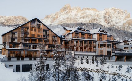 Aman Rosa Alpina resort exterior with snow-covered alpine peaks behind, winter setting.
