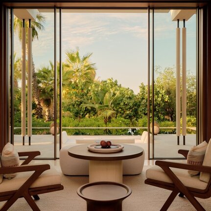 Living area at Amanvari with circular fireplace, mid-century chairs, and views across the estuary to palm trees.