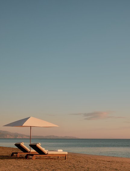 Two sun loungers and parasol on Amanvari's beach at sunset.