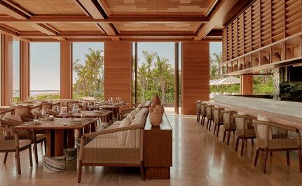 Amanvari dining venue with wooden interiors, floor-to-ceiling windows overlooking Mexican landscape, and contemporary furnishings.