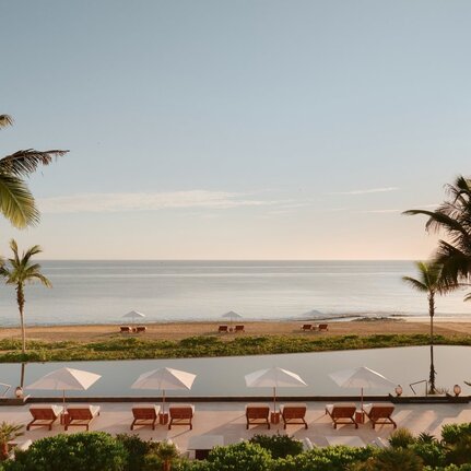 Amanvari's main pool overlooking the ocean at dawn, with palm trees and loungers on either side.
