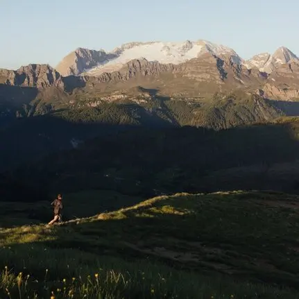 Runner on a mountain trail at Aman Rosa Alpina resort, with Alpine peaks beyond.