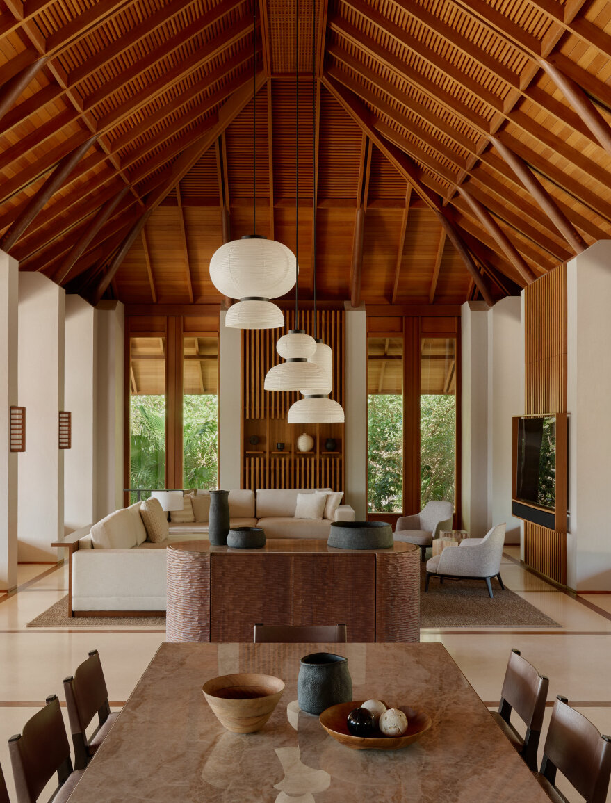 Villa living area at Amanyara resort with pitched wooden ceiling, pendant lights, and floor-to-ceiling windows overlooking tropical grounds.