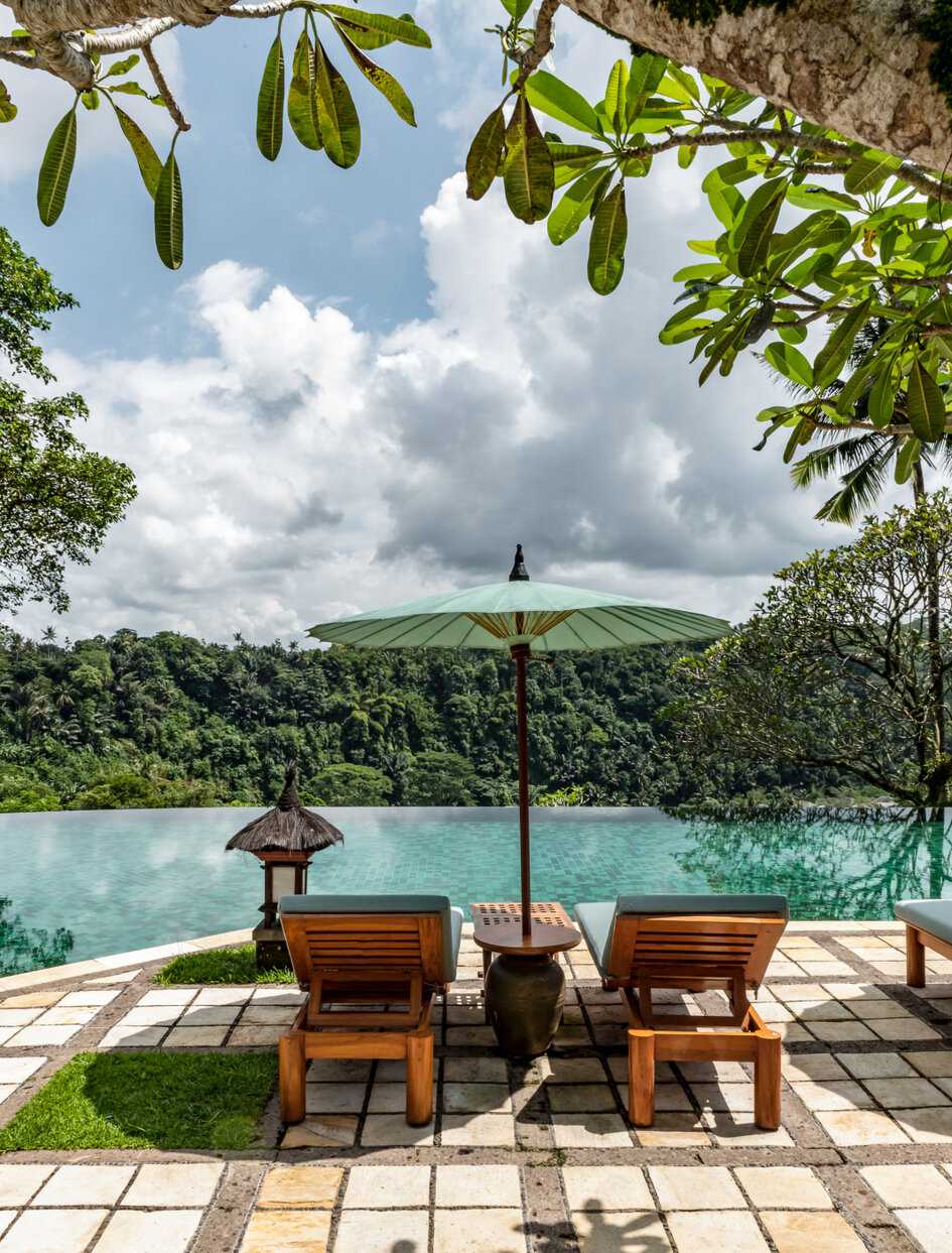 Amandari resort میں دو لکڑی کی کرسیوں کے ساتھ پول کے کنارے شیڈ والا بیٹھنے کی جگہ۔