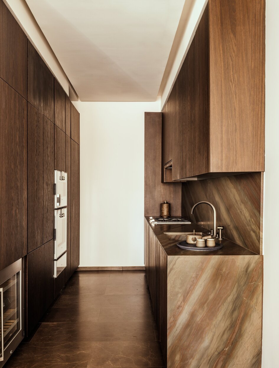 Galley kitchen with wooden cabinetry and dark flooring at Aman New York.