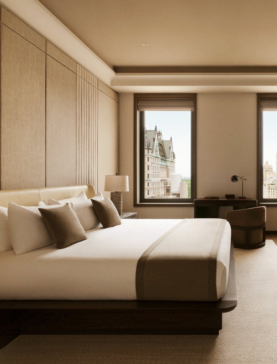 Principal bedroom at Aman New York with floor-to-ceiling windows, cream-upholstered bed, and warm neutral tones.