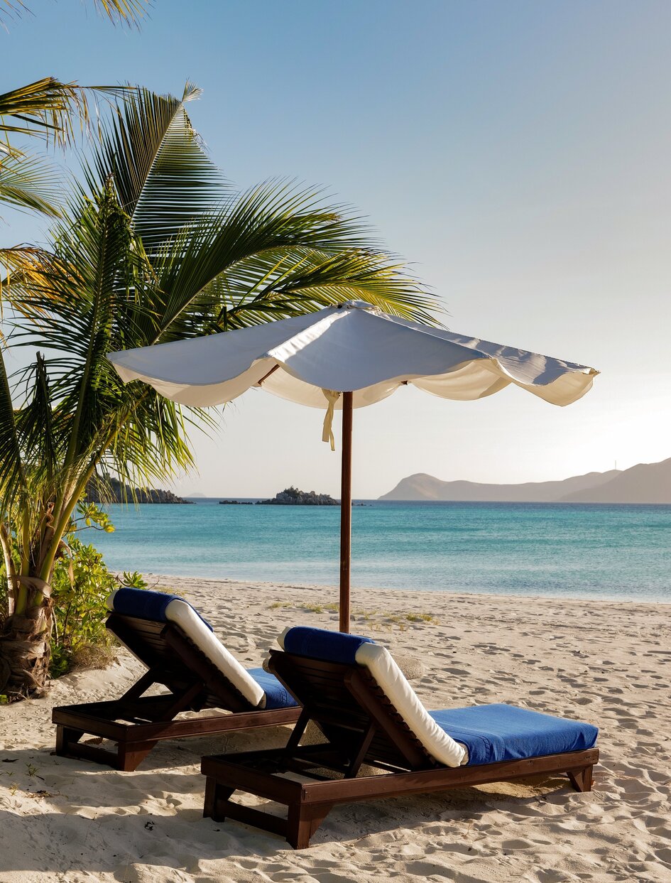 Lounge chairs and parasol on white sand beach at Amanpulo, Philippines, with turquoise water beyond.