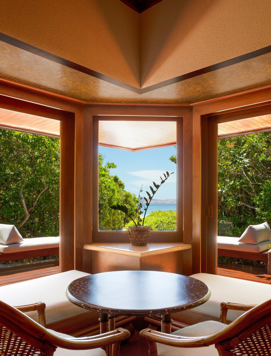 Beach Casita interior at Amanpulo with corner windows framing tropical views and wooden furnishings.