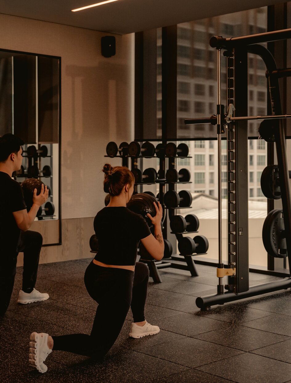 Personal trainer instructing client on weightlifting technique at Aman Nai Lert Bangkok gym.