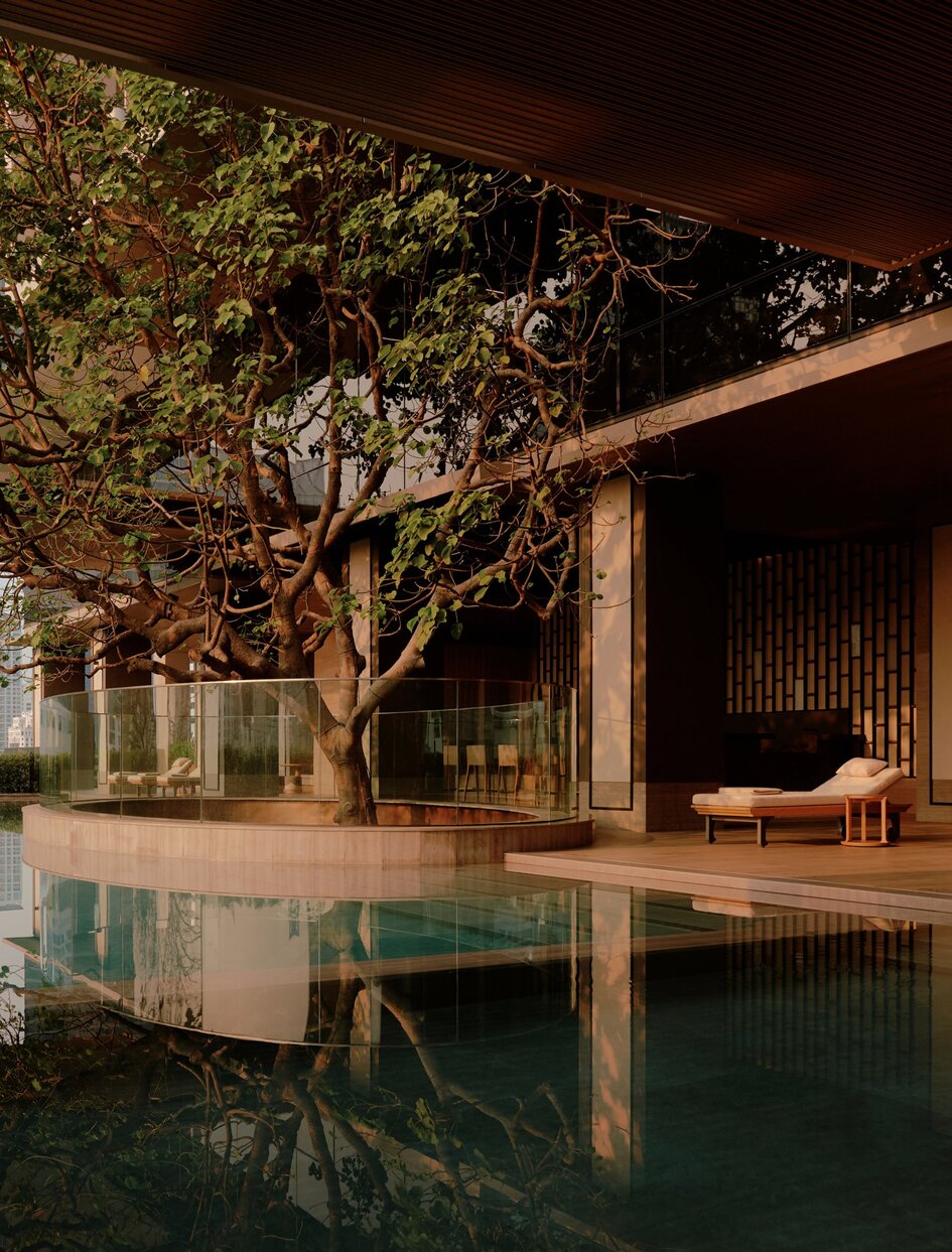Swimming pool at Aman Nai Lert Bangkok at night, reflecting illuminated tree and wooden pavilion.
