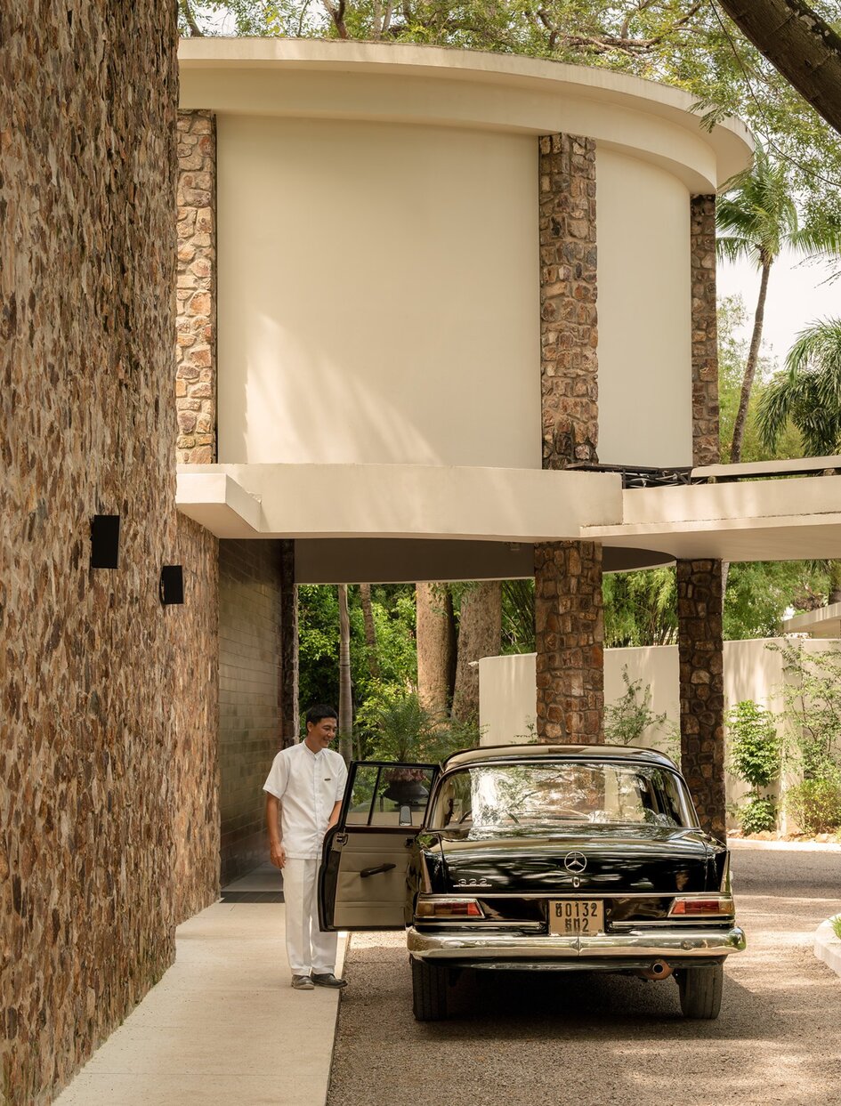 Shaded corridor at Amansara leading to the main pool, with stone pillars and tropical greenery visible beyond.