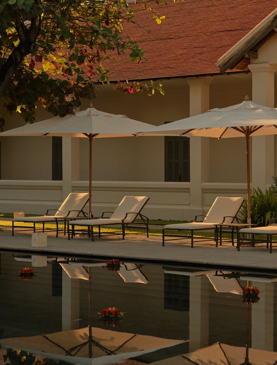 Loy Krathong ceremony at Amantaka's pool terrace at dusk, with cream sun loungers and umbrellas reflected in still water.
