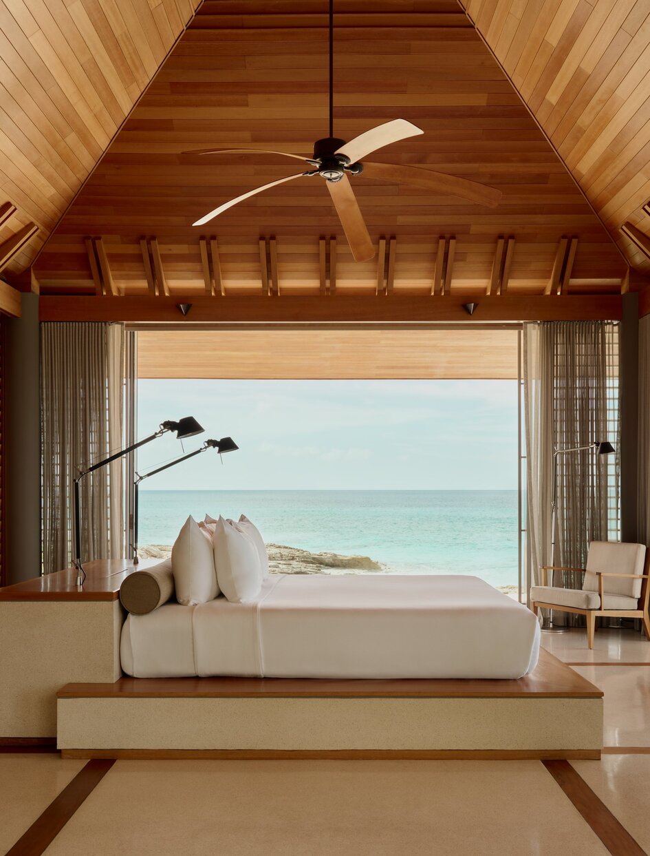 Villa bedroom at Amanyara opening onto a turquoise Caribbean sea view, with ceiling fan and wooden architectural details.