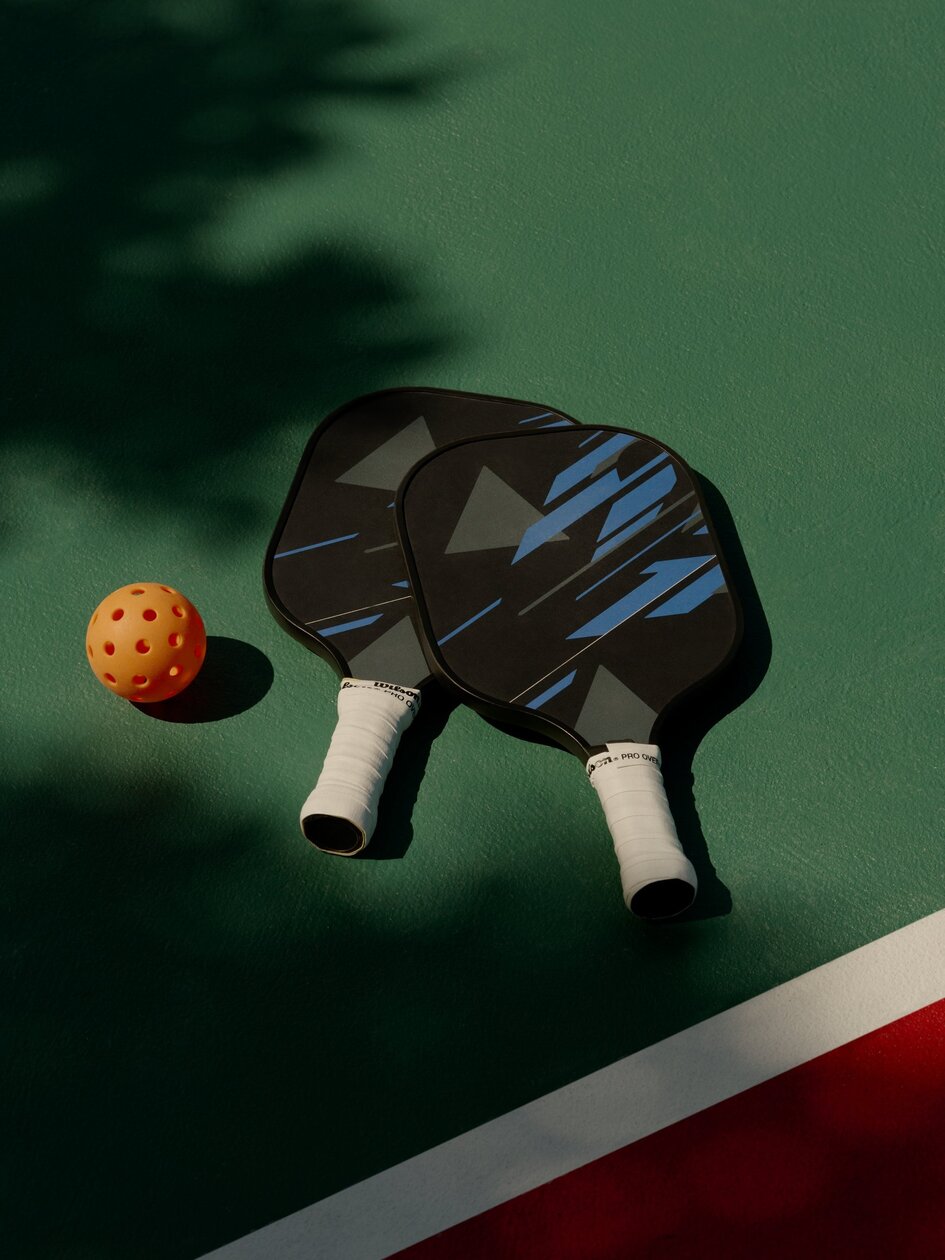 Two pickleball paddles and ball on a green court at Amanyara.
