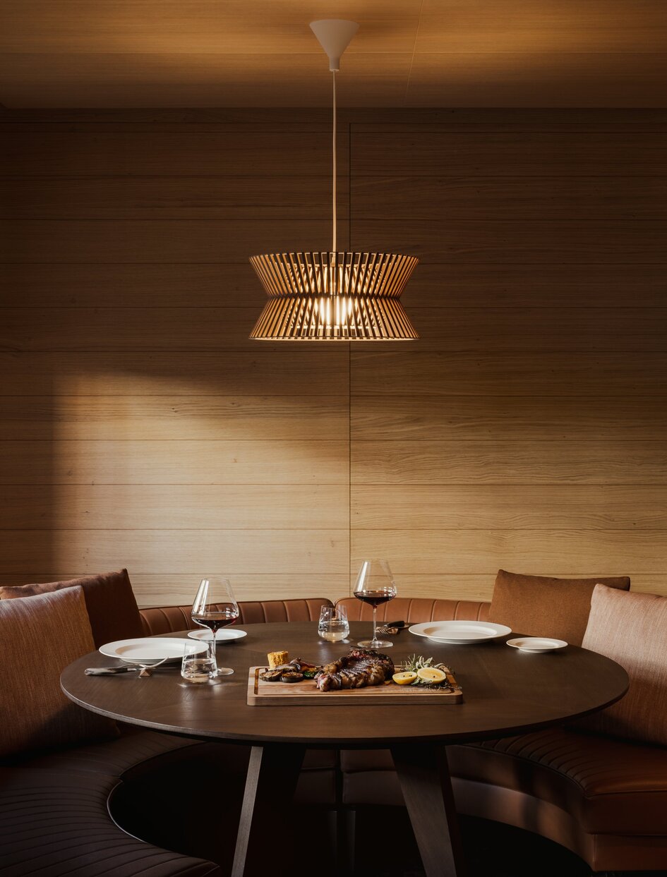 Warm pendant light illuminates a round dining table at Aman Rosa Alpina, Italy.