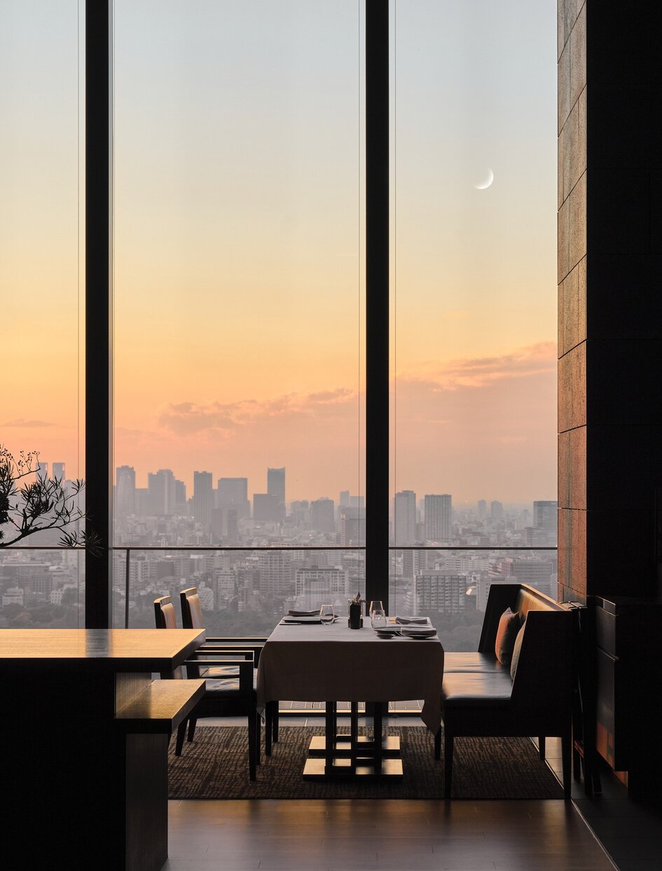 アマン東京のホテルの客室から、夕焼け空と東京の街並みを眺める大きな窓と家具。