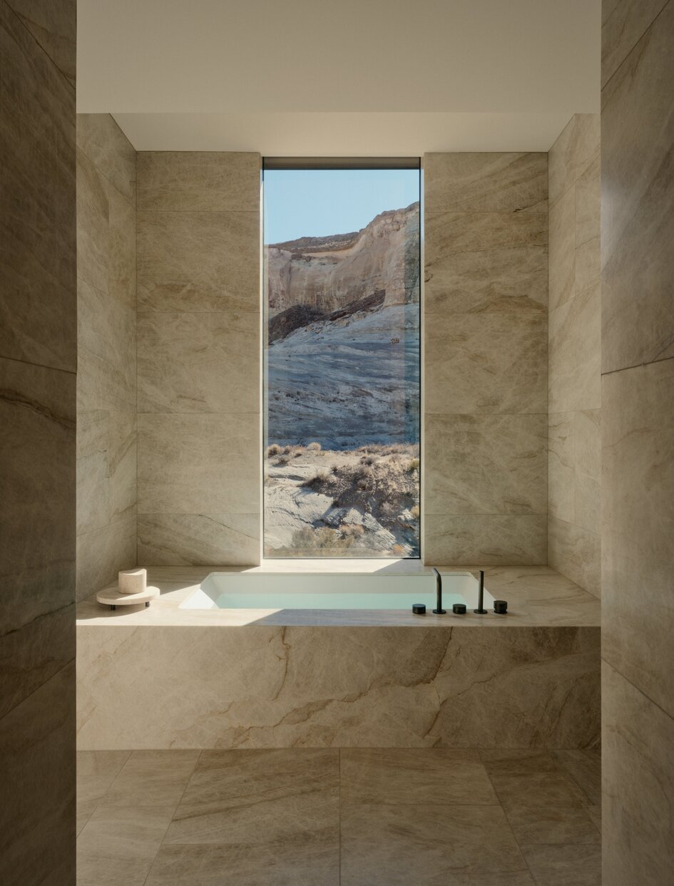 Amangiri six-bedroom villa primary guest suite bathroom with travertine walls and window overlooking desert landscape.