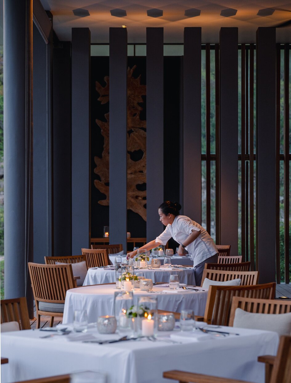 Amanoi's Beach Club Restaurant dining room with wooden chairs, white tablecloths, and vertical timber screens filtering natural light.