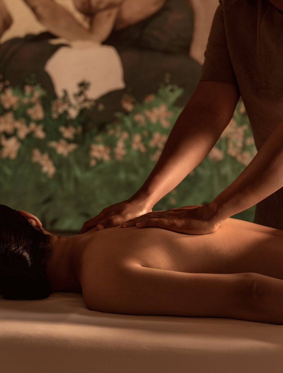 Therapist performing a massage treatment in a spa room at Amanoi, Vietnam, with warm lighting and green botanical elements.