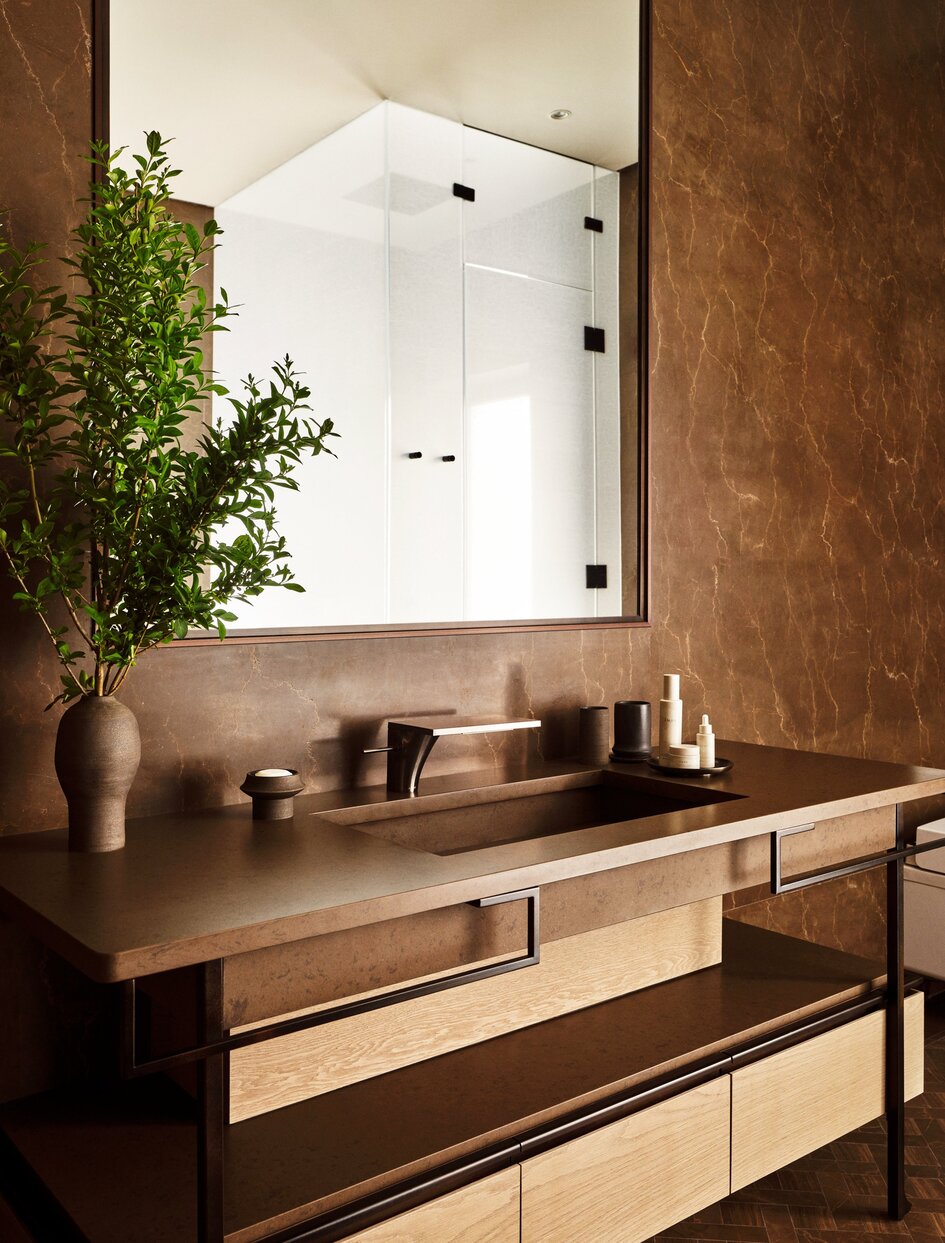Bathroom vanity at Aman New York with terracotta walls, wooden cabinetry, and potted plant beside mirror.