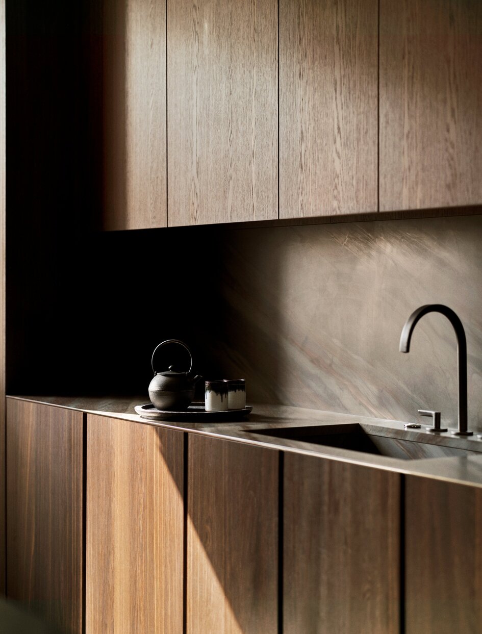 Modern kitchen at Aman New York with natural wood cabinetry and dark countertop.