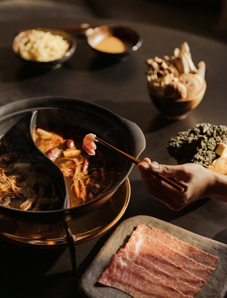 Aman Rosa Alpina: chef's hands preparing Italian cuisine in a dark kitchen setting with ingredients and cookware.