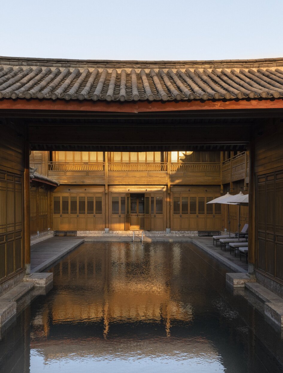 Outdoor swimming pool at Amandayan, framed by traditional Chinese architecture with golden-tiled roof at dusk.