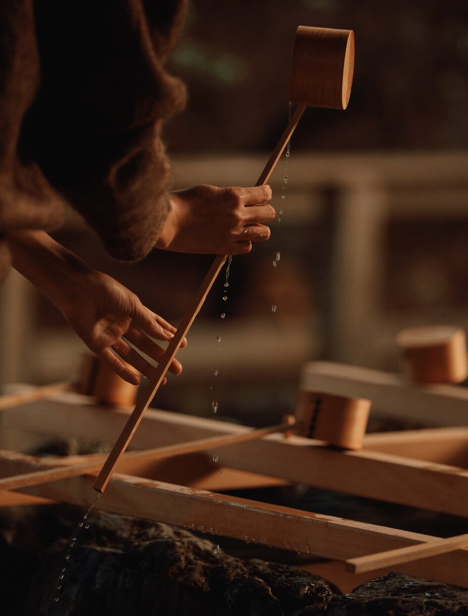 Hands holding wooden tools during water purification treatment at Amanemu resort spa, Japan.