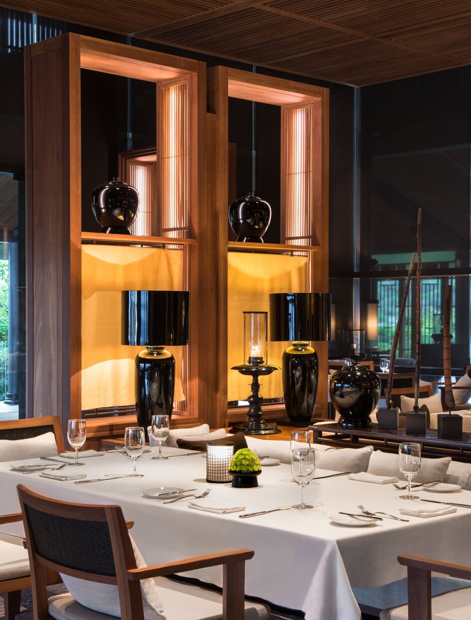 Amanoi's main dining restaurant with set tables, warm wooden cabinetry, and ambient lighting.