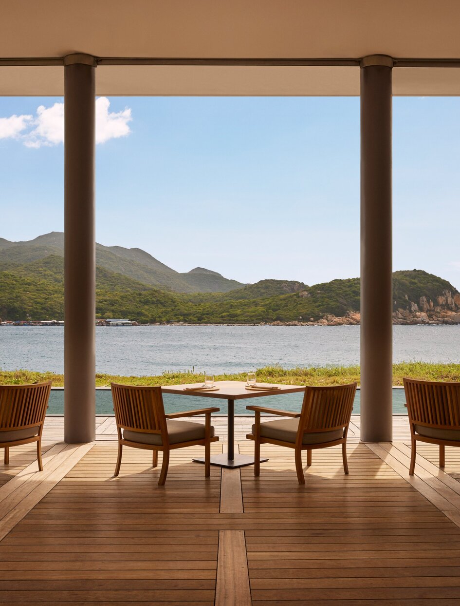 Amanoi beach club restaurant with wooden deck seating overlooking coastal landscape and mountains.
