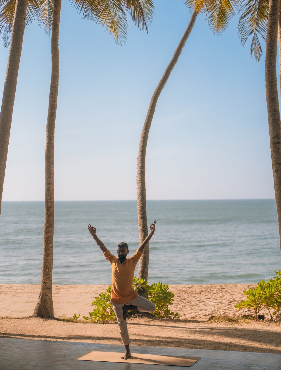 Person practising beachside yoga beneath palm trees at Amanwella, Sri Lanka, with ocean beyond.