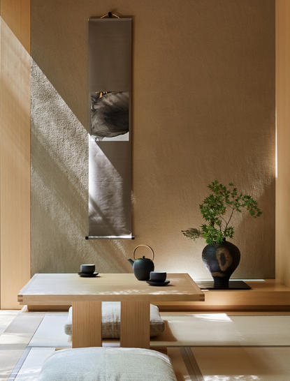 Aman Kyoto pavilion tokonoma with minimalist wooden display table and potted plant against warm ochre wall.
