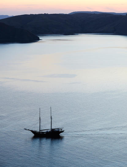 Traditional sailing vessel on still waters at sunset, Amandira, Indonesia.