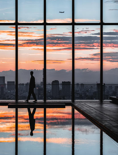 Silhouette of a guest at a floor-to-ceiling window overlooking Tokyo's skyline at sunset, reflected in the glass.