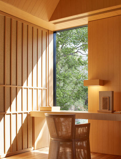 Sunlit suite at Amanemu with wooden writing desk by open doors overlooking forest views.