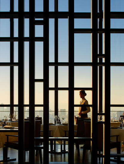 Silhouetted figure by geometric window screens at Aman Tokyo, overlooking cityscape at dusk.