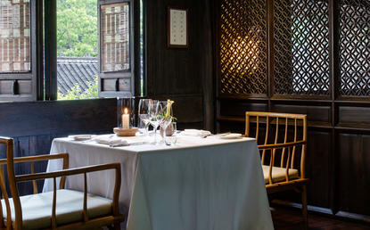 Amanfayun dining room with round table set for service, wooden chairs, and dark panelled walls with latticed windows.