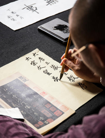 Hand holding brush over traditional Chinese calligraphy at Amanfayun.