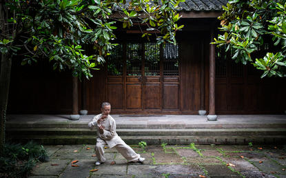 Woman practising yoga on a stone pathway at Amanfayun, with traditional wooden doors and lush greenery in the background.