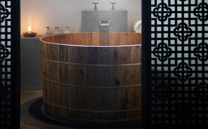 Wooden soaking tub with steam rising, lit by candlelight at Amanfayun wellness retreat.