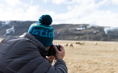 Person in teal hat photographing horses across a meadow at Amangani.