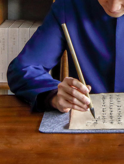 养云安缦度假村南书房，客人身穿蓝色衣服在木桌上挥毫书法。