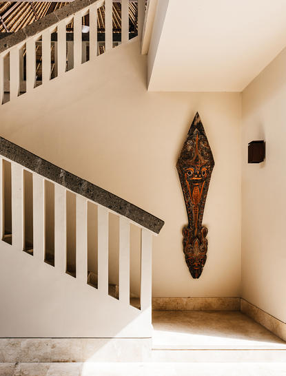 Four-bedroom villa stairwell at Aman Villas at Nusa Dua, with wooden artwork on cream wall.